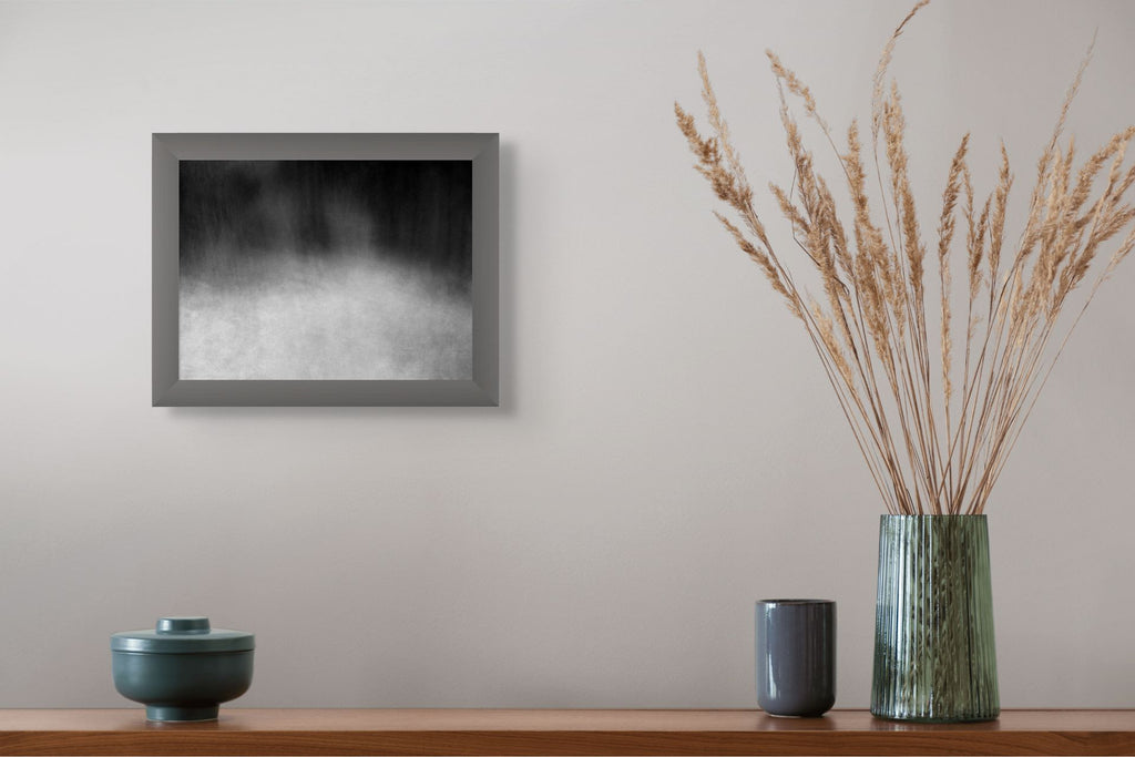 An abstract photo of the woods shot in black and white, framed and hanging on the wall with a vase.