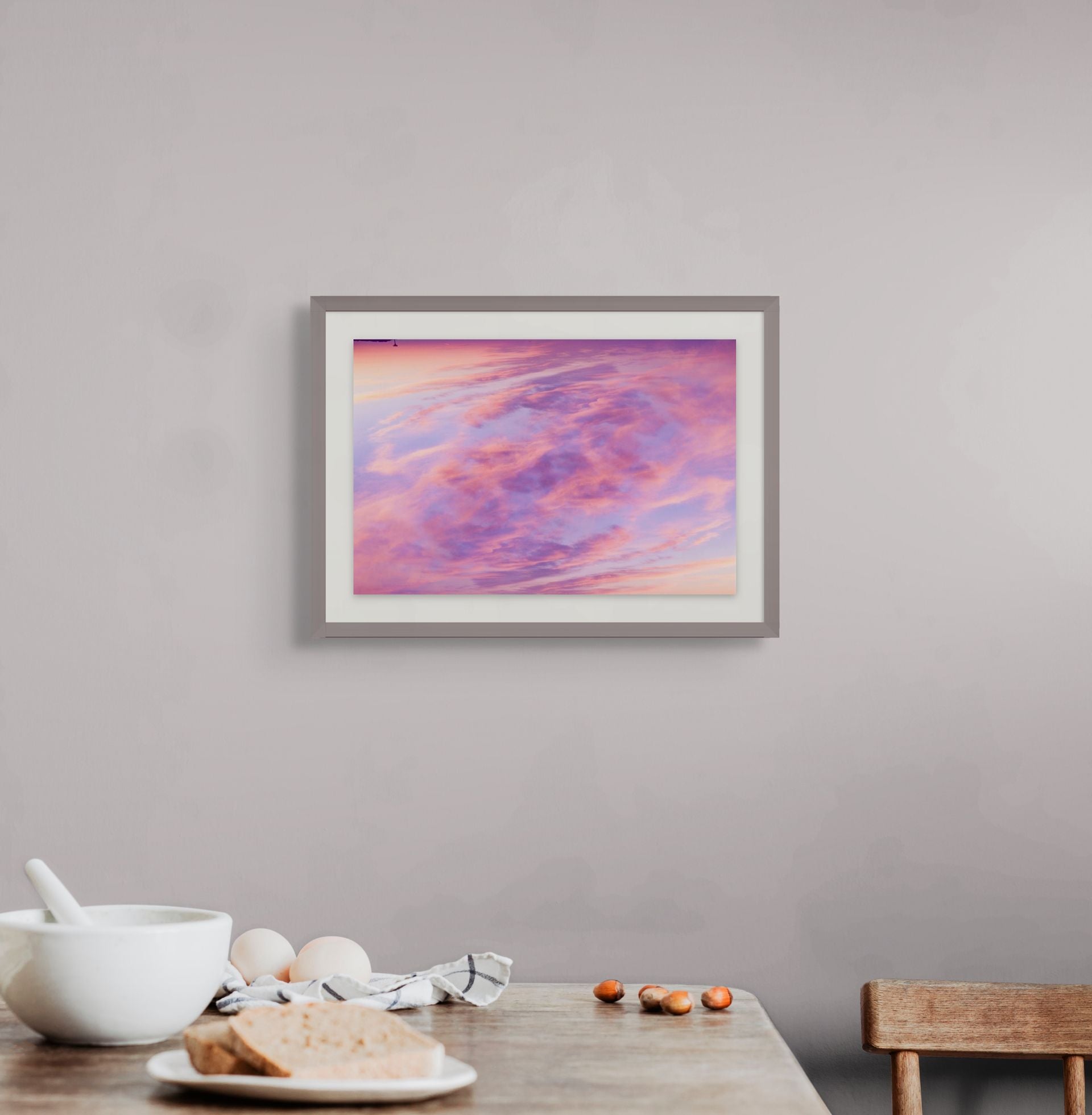 A splash of color in the form of an abstract fine art photograph depicting a double exposure of a sunset sky over cape cod. It is framed and hung on the wall of a kitchen interior.
